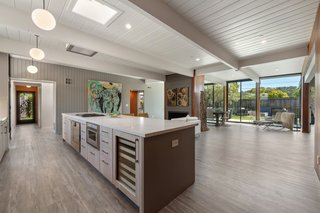 Kitchen, Microwave, Engineered Quartz Counter, Vinyl Floor, Wine Cooler, Ceiling Lighting, White Cabinet, and Pendant Lighting An open floor plan merges the expansive living area. Nine-foot-high walls of glass and a skylight ushers sunlight into the space.