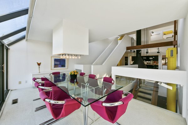 A formal dining area sits at one end of the central living space. The atrium-like space is enclosed by wall-to-wall windows on two sides.