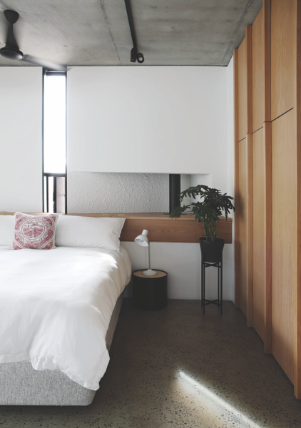 Wooden closet doors and accents warm up the bedroom, which otherwise continues the house’s rough concrete and plaster palette. The bed linens are from The T-Shirt Bed Co., while the lamp and side table are from MRP Home. The planter is from Country Road.