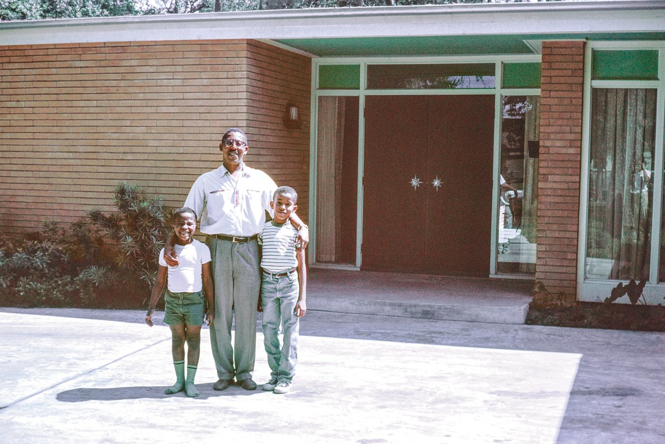 John Saunders Chase stands in front of his family home in Houston, Texas, with two of his three children, Anthony and John Jr. The home is characterized by its low-slung brick form, and an experimental central courtyard that shifted the paradigm for Modernist architecture in Houston.