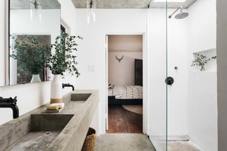 Concrete sinks and flooring complete the modern bath, which is also illuminated by a skylight above the shower.