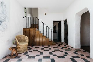 Inside, pale pink tiles line the entryway floor, contrasting with whitewashed plaster walls. The living room is located through an archway on the right, while the kitchen is straight ahead.