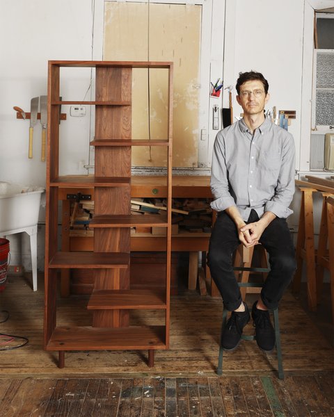 Designer Casey Lurie sits beside a piece from his Everyday Shelving project.
