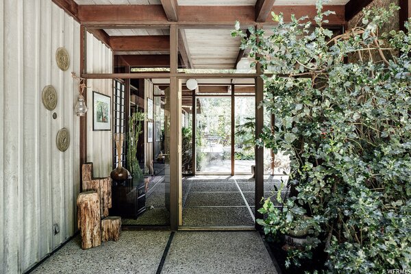 From the gravel driveway, the main entrance opens into a central vestibule, with views of the lush backyard visible through the glass walls straight ahead. Square-shaped slabs of concrete bordered by wood are repeated throughout the interior and exterior.