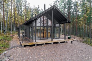 The three-bedroom Iniö model from Pluspuu features floor-to-ceiling windows, a loft-like interior, a wraparound deck, and a gable outline reminiscent of a traditional log cabin.