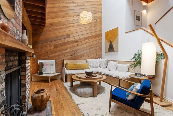 Wood-clad walls continue into the primary living room, complete with tall ceilings and an original red-brick fireplace. The home's central staircase sits to the right.