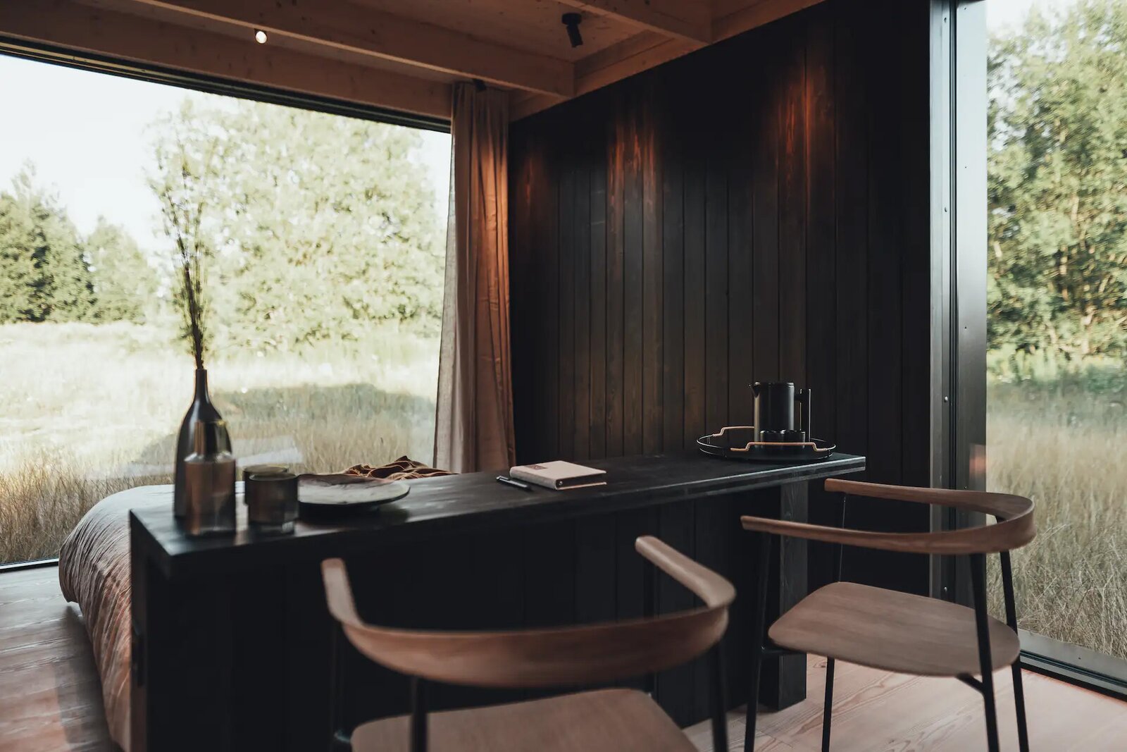 Wrapped in perforated metal and European larch stained a deep-brown color, the rectangular prefab includes an open kitchen and living space, a bedroom, a bathroom, and wall-height windows to take in a view.