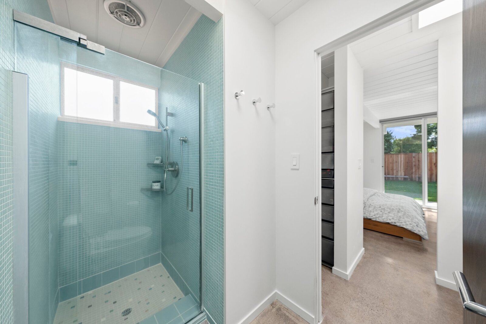 In addition to direct outdoor access, the primary suite presents a large walk-in closet with custom organizers, separate vanity area, and private stall shower lined with mosaic tiles.