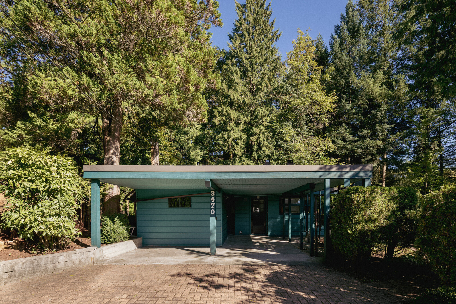 A wide driveway leads to the one-level painted property, the facade of which pops against the encompassing leafy trees.