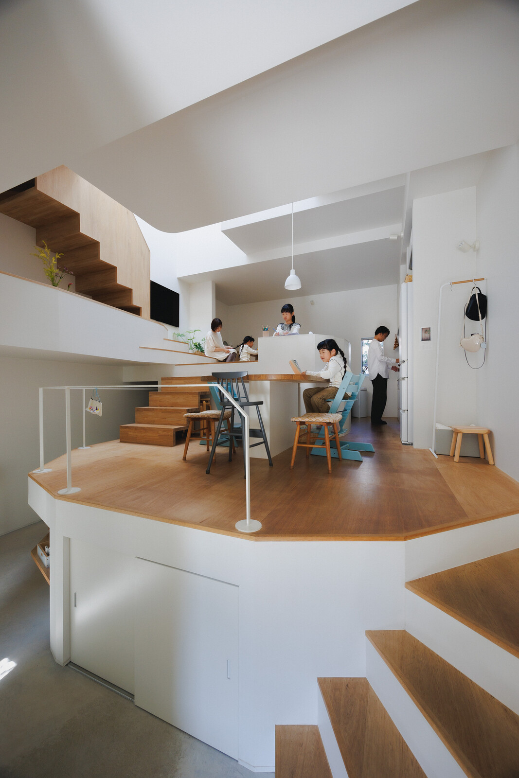 A built-in table and an assortment of chairs in the dining area are among the few pieces of furniture in the home. White paint was chosen to make the interiors brighter, along with matte-white appliances and light-toned woods like Lauan plywood and Japanese ash.