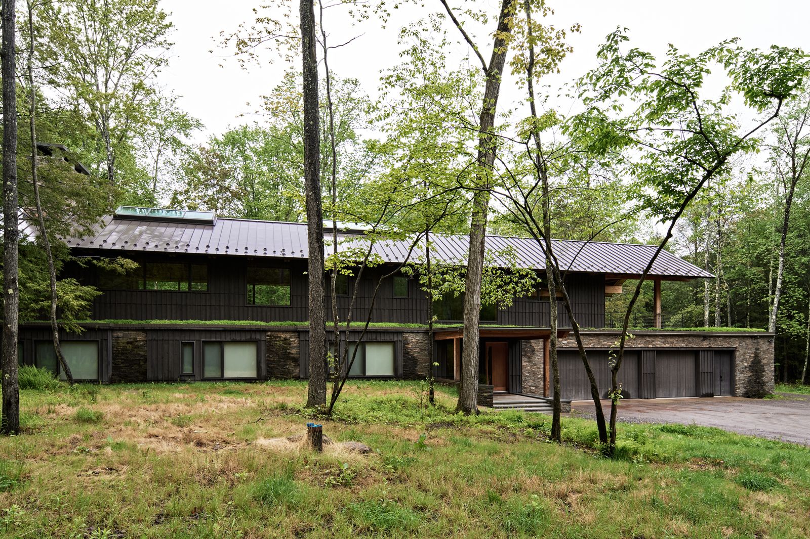 The bedrooms are tucked into the stone-clad lower level, while the upper floor, wrapped in Marvin Ultimate windows, opens up to the canopy. The planted roof insulates the lower level while helping the home recede into the landscape.