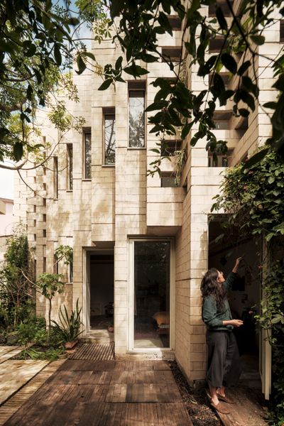 Artist Jimena García Álvarez-Buylla stands outside the pleated brick facade of her home and studio on the outskirts of Mexico City. The triangular building, designed by Estudio MMX, is set amid greenery on the same plot of land where Jimena grew up and her mother still lives. An open-layout ground floor holds a living area, a sleeping area, and a kitchenette.