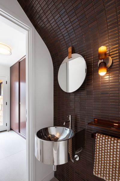 Burgundy Heath tile envelops one wall in the powder room, which is part of the entry. The industrial-style polished steel sink is from Lacava and the sconce is by In Common With.