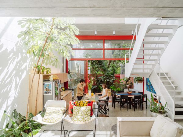 The polished concrete floor inside gives way to a brick patio and a garden behind the house. Two embaúba trees grow up the atrium from indoor beds in the living room. The Atibaia counter stools and Eclipse dining table are from Casa Paulo Alves. The Tiza chairs are from Del Portillo. The C11 white sofa by Marcus Ferreira is from Carbono, and the metal-framed lounge chairs are from Paulo Mendes da Rocha. The metal planter is from AMP. The kitchen cabinetry was designed by Arkitito.


