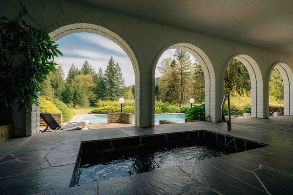 The covered terrace (complete with a hot tub) frames the pool and forest through a row of white arches. According to the current owners, the original owner-builder constructed the pool and the arches before the house itself 