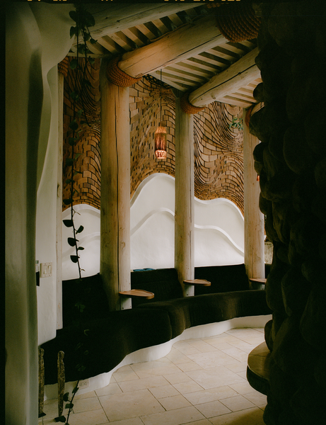 Through the front door and off to the left is the lounge, which has a hearth nested within the home’s river-rock core. The wavy white wall was originally covered in cascading, plush seating.