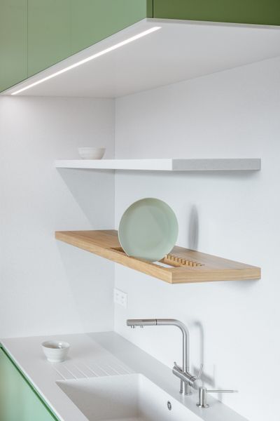 The apartment now revolves around a central green core, which integrates the kitchen, built-ins for storage, and a wardrobe. A backsplash and counter in engineered stone contrasts the core’s lacquered MDF.