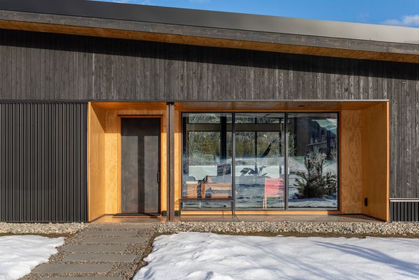 Black stained cedar board-and-batten siding creates a warm, carved-out entry alcove against the home's black corrugated metal exterior—a material chosen partly for its fire resistance in the valley.