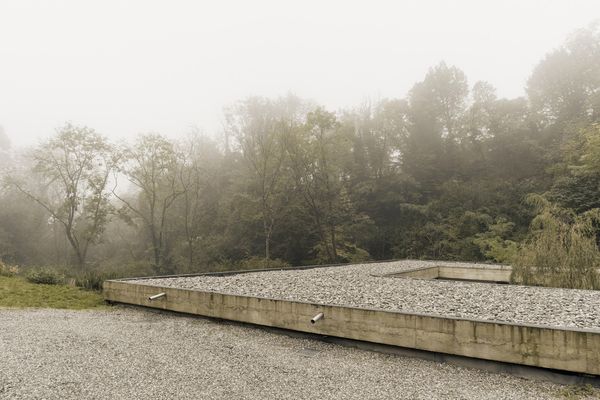 Designed by Lorenzo Guzzini Architecture between 2021 and 2024, Narrow House is a 125-square-meter home in Tavernerio, in the hills just outside Como. The property sits above a stream on the edge of a wooded valley. Viewed from the street, <a href="https://eumiesawards.com/heritageobject/narrow-house/#description-section">the flat roof is covered in stone and pebbles</a>. The approach descends through the site toward the courtyard and house below.