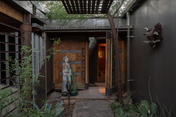 A recessed entry beneath a steel trellis leads into the house, where the living, dining, and kitchen areas are arranged straight ahead, with the two bedroom suites on opposite sides.