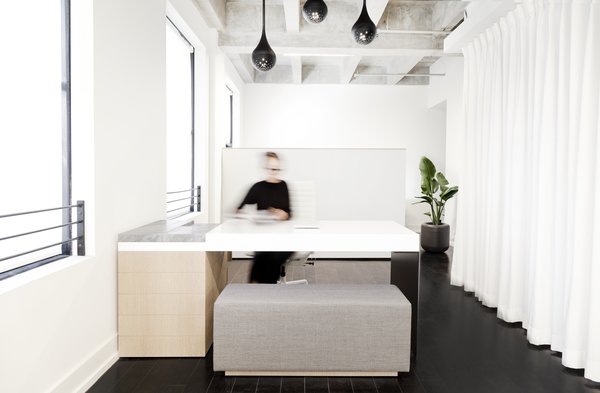 The custom appointment desk was designed and built by using a single bent sheet of aluminum, lacquered MDF, marble, and white oak. The floor-to-ceiling white textured curtain hides a built-in kitchen and brings a softness to the space.