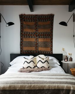 CB2 was also a major furnishing source in this bedroom, as the lighting and matching patterned pillows were found there. The striped throw at the edge of the bed is from Etsy.