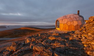 The small cabin's cross-laminated timber (CLT) shell, composed of 72 unique wooden panels, is designed to withstand severe arctic storms and heavy wind conditions.