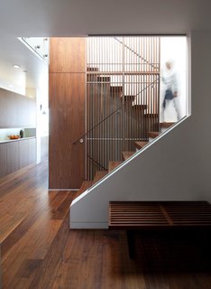 A slatted walnut screen is a centerpiece of the home’s new design. Accentuating the height of the space, the vertical slats come together with metal rods and a sleek handrail, creating a graphic manipulation of positive and negative space. In addition to allowing light to permeate the interior, the screen is visible from most vantage points in the home, providing an anchor of visual interest.