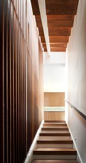 The reimagined entry stair favors rich and warm walnut hues, leading visitors to the relocated third-floor kitchen.