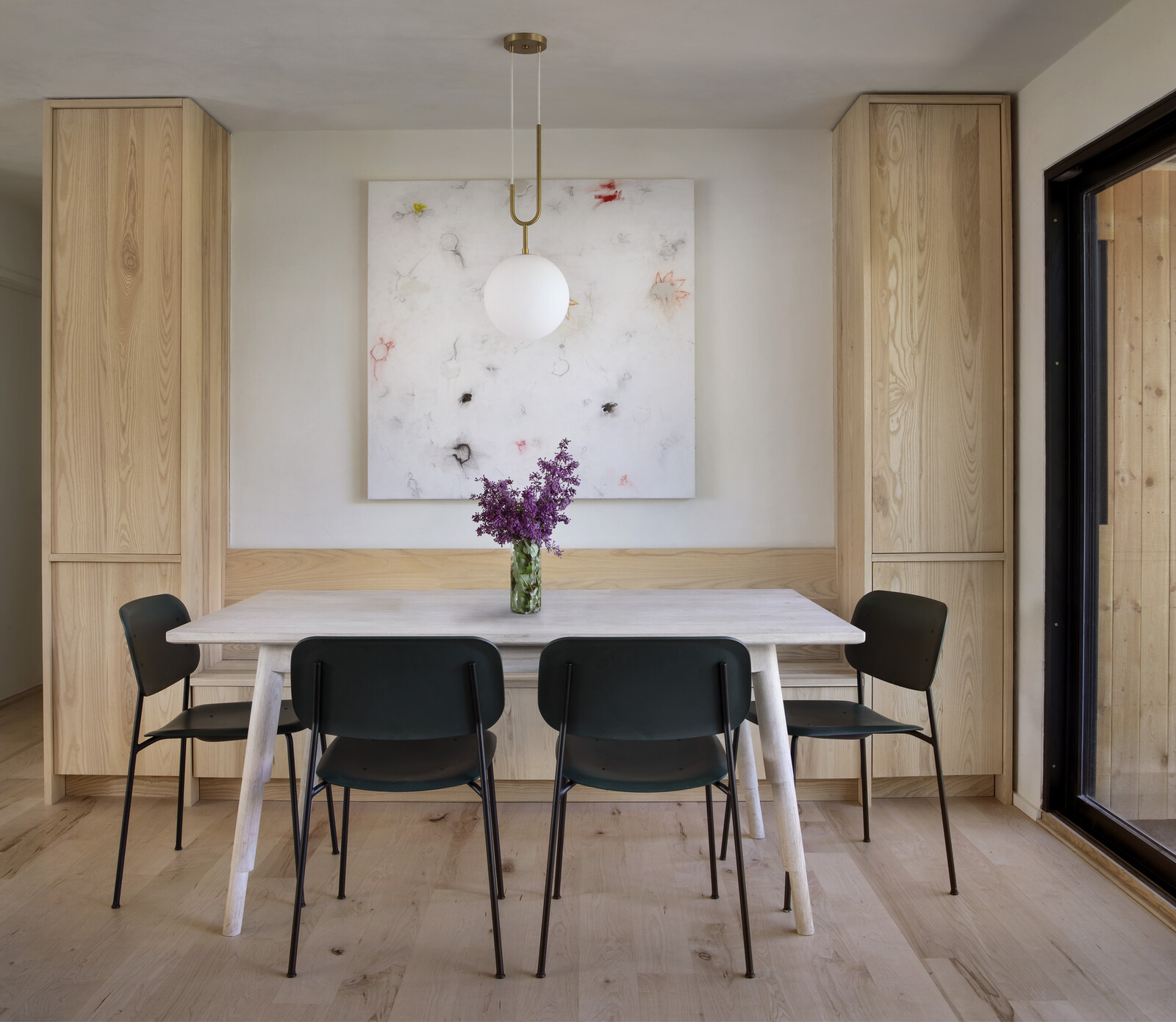 A Nash Martinez light fixture hangs over a whitewashed ash dining table by Robert Rahm of Marrow, with a Sandra Dal Poggetto artwork between the cabinets.