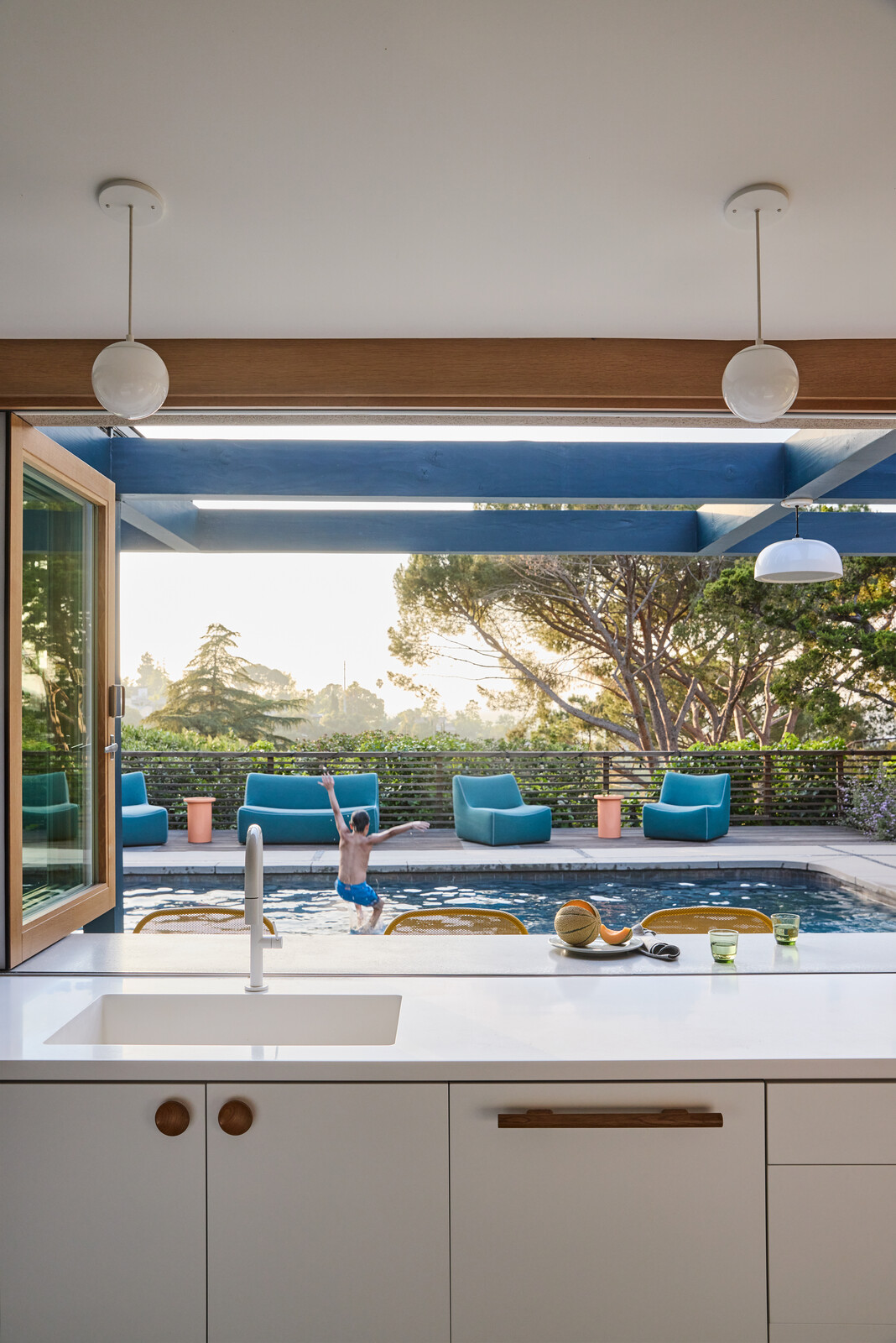 The new kitchen's sink (with a California Faucet fixture) and Corian counter open through operable La Cantina windows onto the pool area and an outdoor extension of the counter. Just beyond, David and Laurie's son Asher takes a plunge.