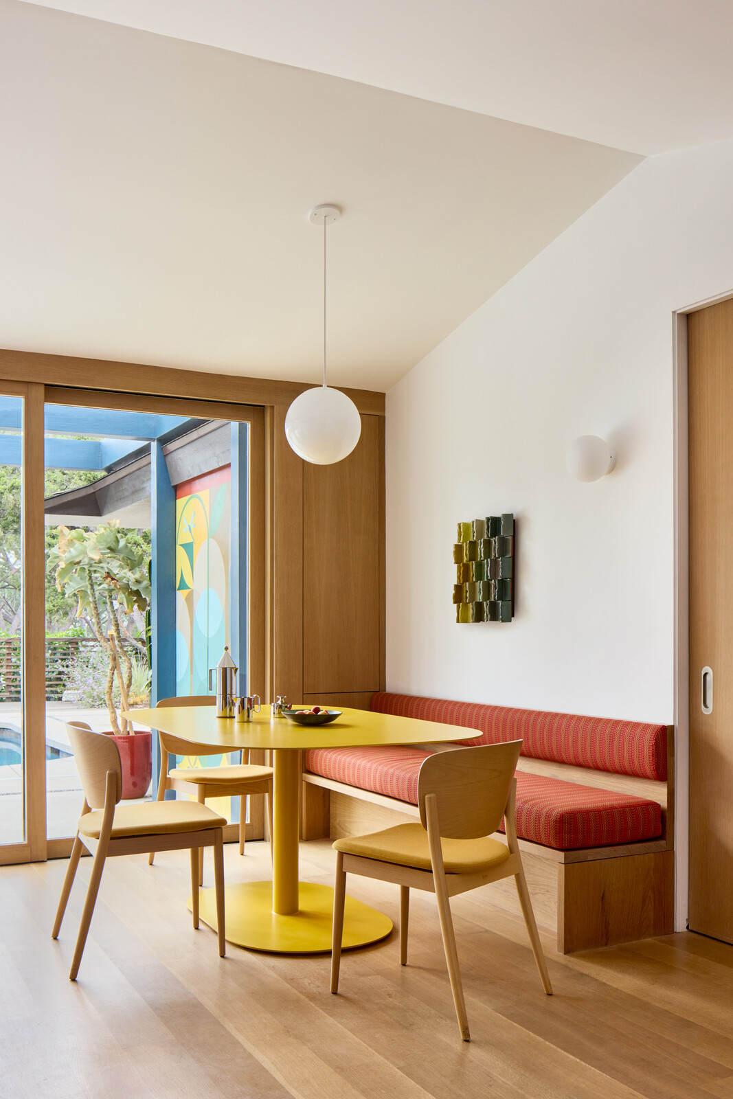 The new breakfast nook pairs a custom bench and table, both manufactured by Maneuverworks and surrounded by DWR Valencia chairs. Above are a Flos wall sconce and Schoolhouse Electric Luna pendant light