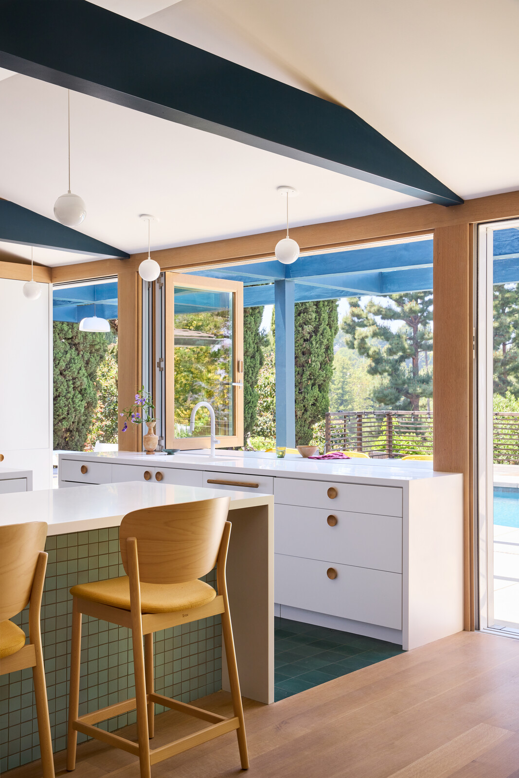 To bring color to the mostly-white kitchen, Chet Architecture's design took color inspiration from the landscape outside, be it blue from the pool for beams and the trellis, or green from the cypresses for the Villa Lagoon concrete tile.