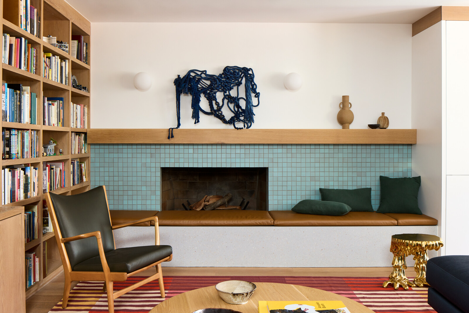 The new den's rebuilt fireplace is clad with the same Heath Ceramics tile as the kitchen island. Avove it is a Christopher Wrobleski rope hanging. A vintage Hans Wegner chair with Maharam leather cushions was paired with a Lawson Fenning San Rafael Paolo coffee table.
