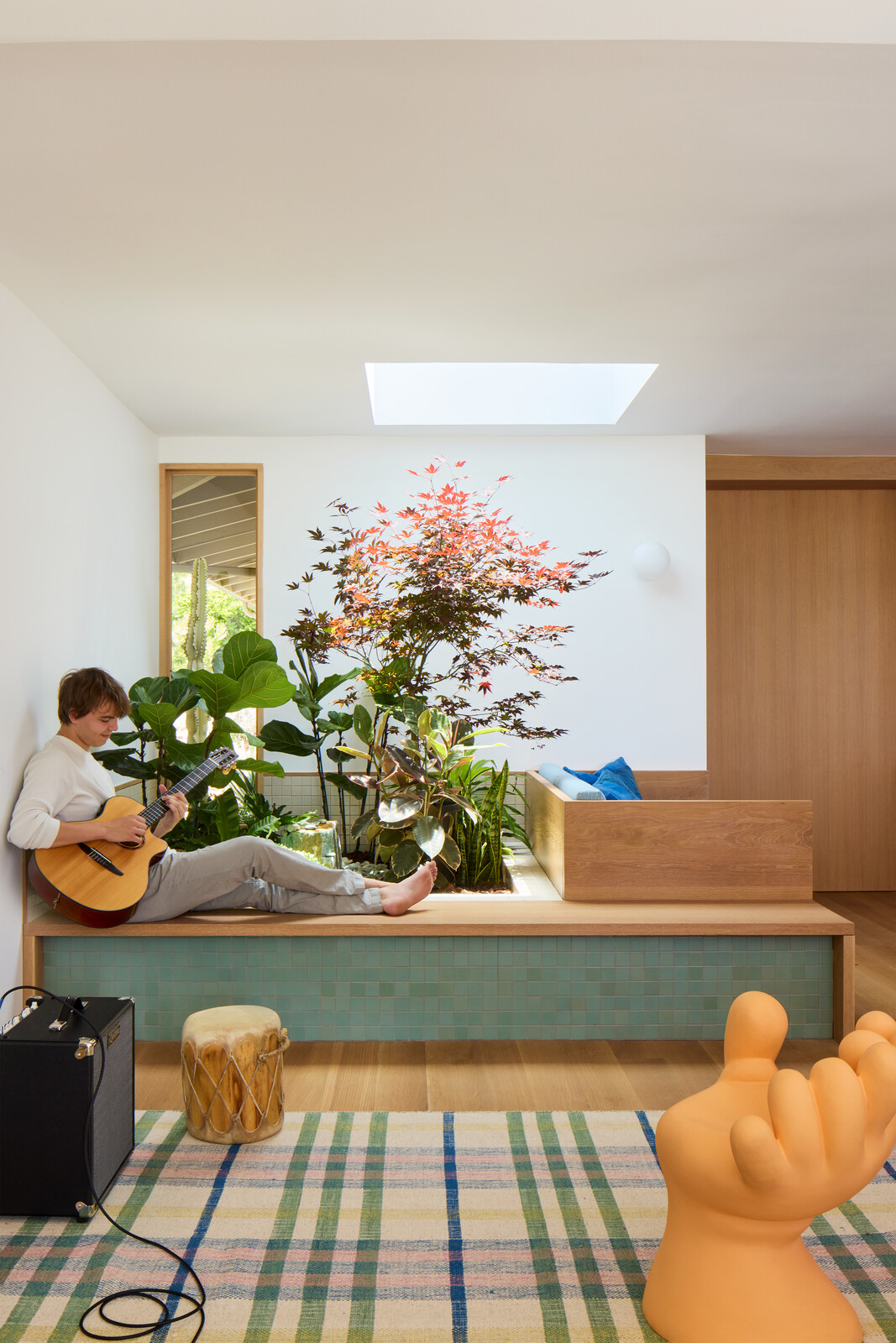 David and Laurie's son Noah plays guitar on a custom bench beside the indoor garden. A Haas Brothers stool sitas atop a Kneeland CO. X Temple rug in a Vanora pattern.