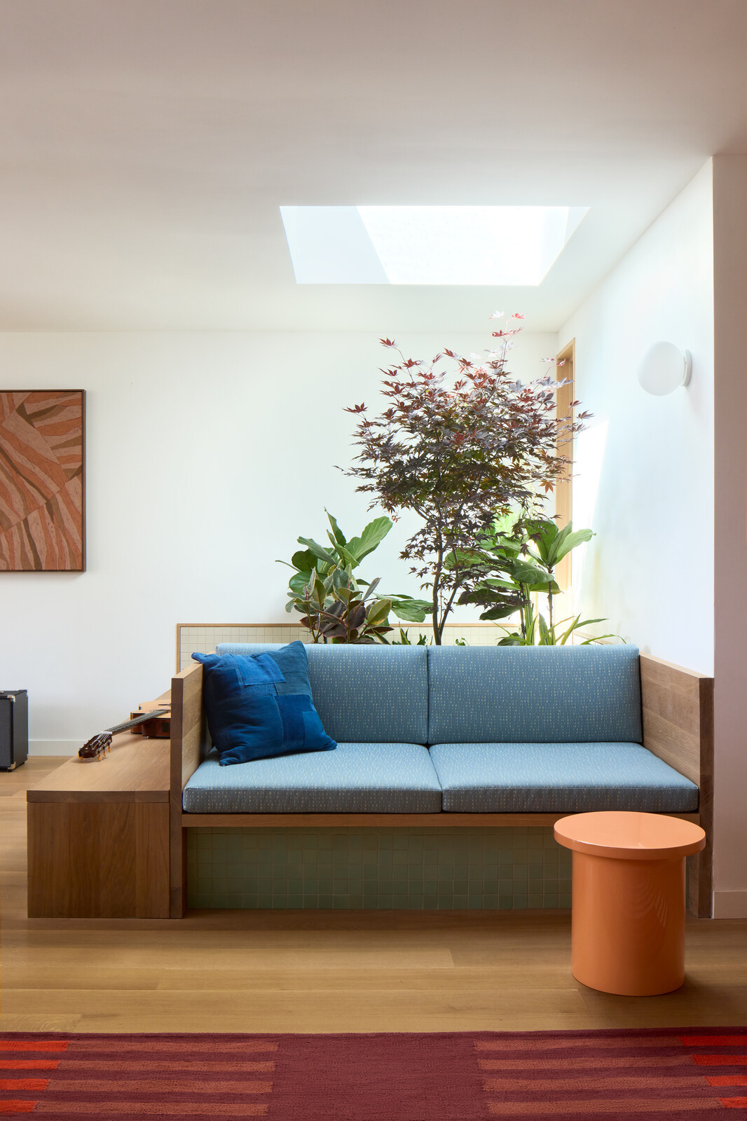 A custom bench was built into the indoor garden, its cushions made with Rebecca Atwood fabric and complemented by a Christopher Wrobleski patchwork pillow as well as a Mondos side table. The wall painting is by Abel Macias.