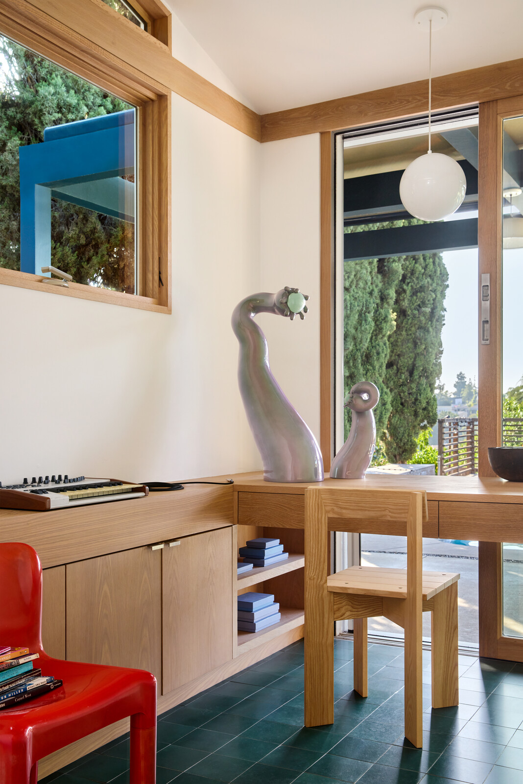 A small home office, also overlooking the pool and patio, was built just beyond the kitchen, with the same Villa Lagoon concrete tile flooring. The custom desk is paired with a vintage Kartell red Chair and a Ferm Living Ark dining chair.