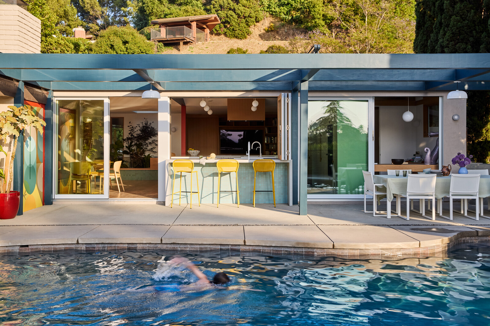 An extended trellis helps shade the patio. Yellow Emu Living stools sit below the operable La Cantina doors. At right are an outdoor table and chairs from DWR's 1966 series.