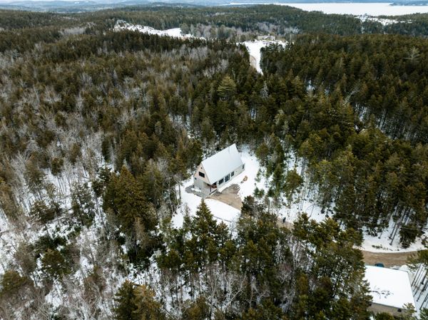 The home occupies a 12-acre wooded property, a short drive from the coast of Penobscot Bay (seen at the top of the photo). At the bottom right is an existing single-room cottage that was moved from near where the new house now stands.
