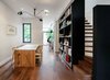 Modern home with Dining Room, Ceiling Lighting, Bar, Storage, Chair, Table, Medium Hardwood Floor, Stools, Recessed Lighting, Shelves, and Pendant Lighting. On the ground floor adjacent to the open living and dining room, a tall black bookcase defines the stair, housing the owners’ colourful books and small collectibles. Photo of Contrast House