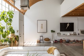 Raw concrete floors and wood beams and arches provide an industrial aesthetic in the loft, where designer Sally Breer arranged a custom sofa covered with linen cotton and a Laurel brass floor lamp. The lightning bolt painting is by Breer's mother. 