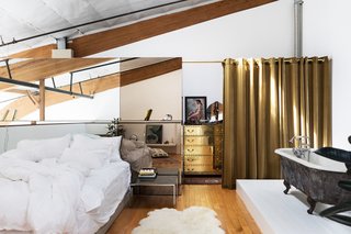 Breer designed a glass wall to section the closet and act as a headboard in the bedroom area, where a black clawfoot tub is across from the bed. The gold dresser is vintage Sarreid. 