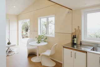 The dining area, flooded with natural light due to strategically placed windows, is flanked by the living room and the kitchen. Plywood wall panels provide warmth and texture for the space.