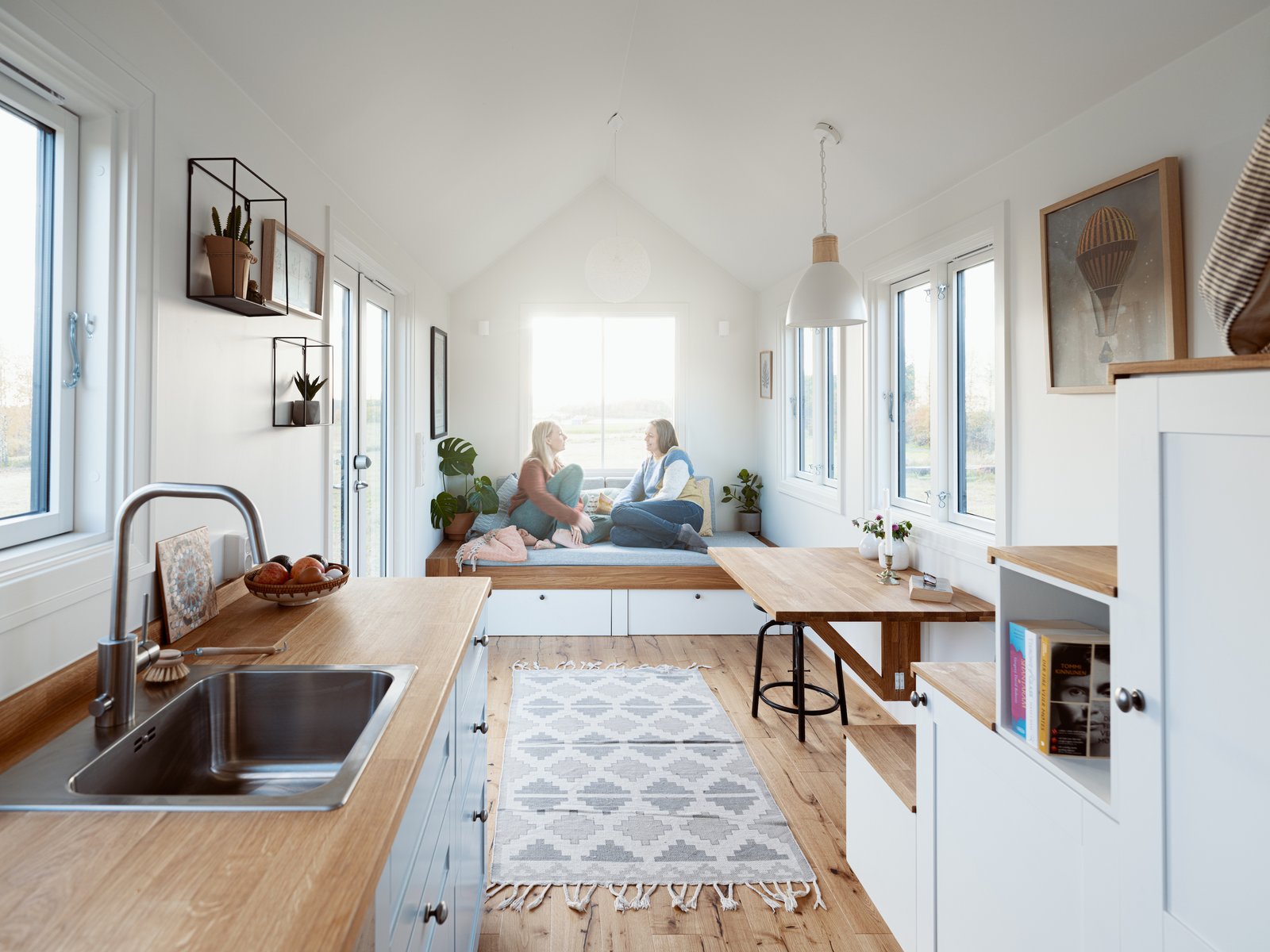 White-painted walls and cabinetry are offset by pale wood kitchen counters, stair treads, and flooring to maintain Scandinavian design aesthetics as well as a light and airy feeling for the interior. 