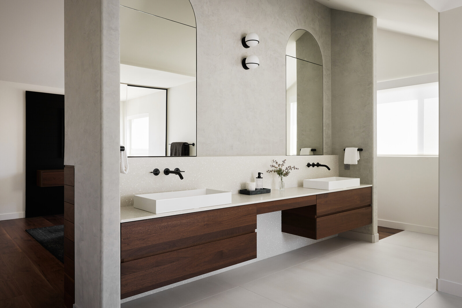 A floating walnut vanity and arched mirrors provide a calm quality for the primary bathroom.