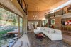 Modern home with Living Room, Medium Hardwood Floor, Pendant Lighting, Coffee Tables, Sofa, and Recessed Lighting. Sliding glass doors open the lower-level living room to the outdoors. Stone steps bridge the sunken biofilter pond surrounding the home. Photo 4 of A Sustainable Mountain Home in Chile Asks $1.36M