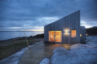 Designed by TYIN tegnestue Architects and built by the owners themselves, this cottage celebrates traditional back-to-nature elements in traditional Norwegian culture. Situated amidst marshland, sea-adjacent rock, and scattered pine-and-juniper vegetation, careful consideration was made to protect the sensitive surrounding terrain. Only 328 feet from the sea, some marsh had to be cleared while preparing for the construction, exposing bedrock—which integrated the cottage into the landscape.