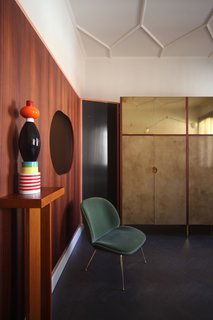 This corner of the space features a Beetle dining chair by Gubi, a totem by Ettore Sottsass from Arts & Crafts Gallery in Venice, mirrors by Atipico. The incredible boisery consists of eucalyptus wood, glass, brass, lacquered iron, and "stucco veneziano" by Marcante-Testa, built by Materia Design and Om Project. The Saraille wallpaper is by Designers Guild while the ceiling frames were designed by Marcante-Testa and built by Orseolo Restauri. 