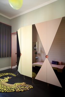 This funky bedroom features a Salamandrian carpet by JIWONXKIM, a blow-suspended lamp by &Tradition, a Tam Tam floor lamp by Marset, and a wardrobe made of lacquered-MDF and pink mirrors. It partially hides a stacking bed by Muller Mobelweskstatten.
