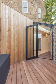 The patio area floor is finished with a dark-stained decking, surrounding and contrasting the pale plywood. 